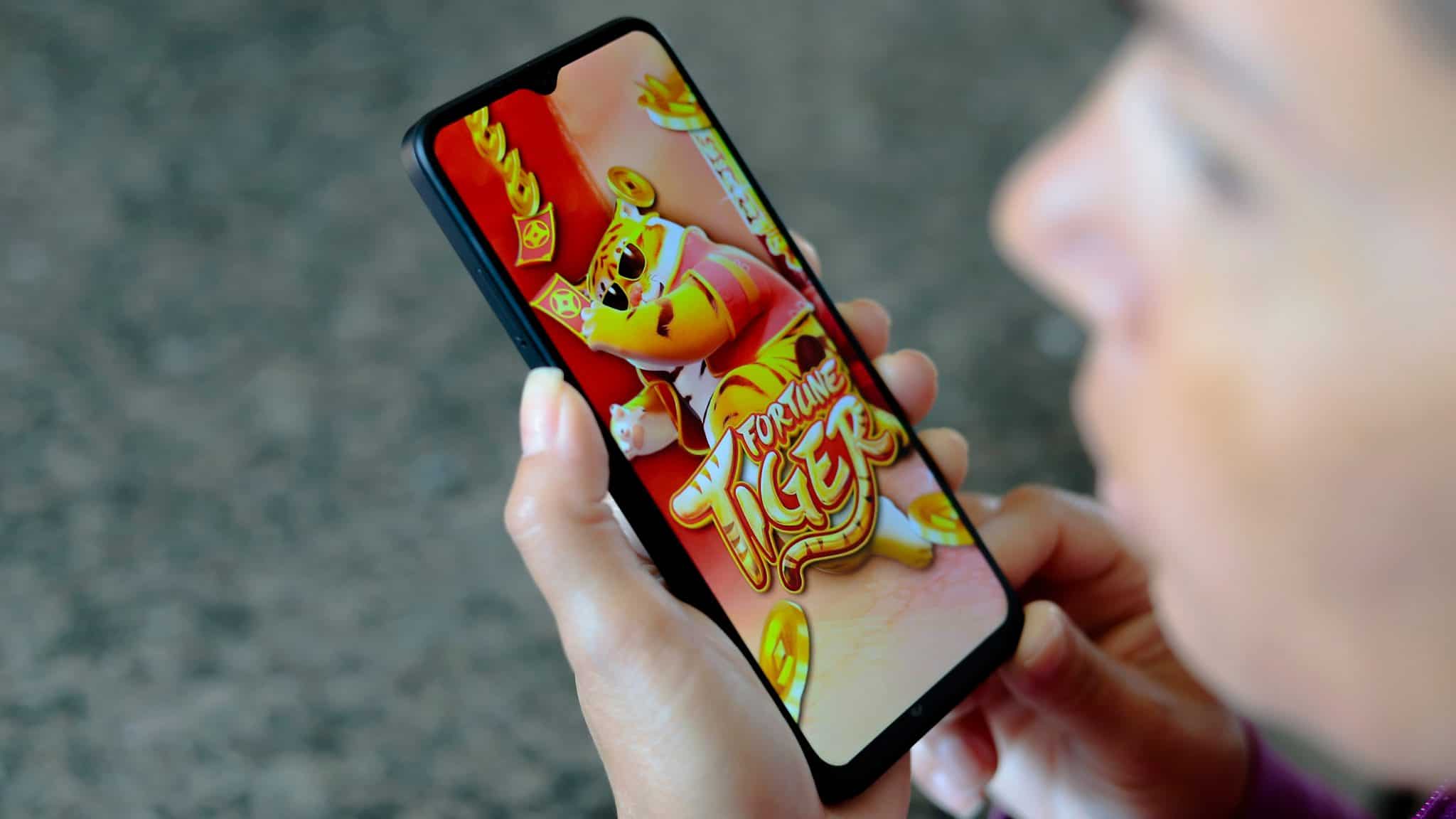 Pessoa olhando para o lado enquanto segura celular com jogo do tigrinho aberto