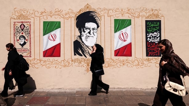 Iranians walk past a wall decorated with the image of assassinated Iranian supreme leader Ayatollah Ali Khamenei