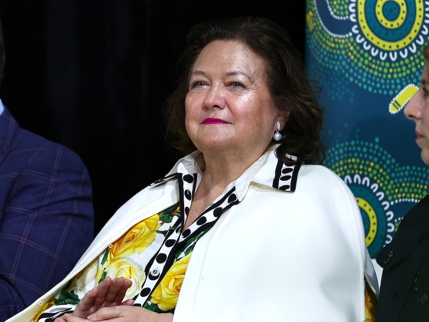 a middle-aged woman wearing a white blazer sitting inside an aquatic centre