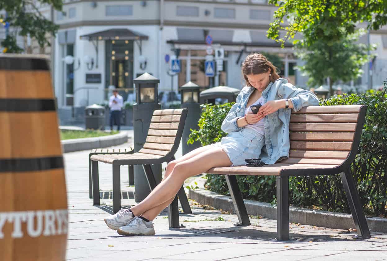 adolescente sentada em uma praça olhando o celular.