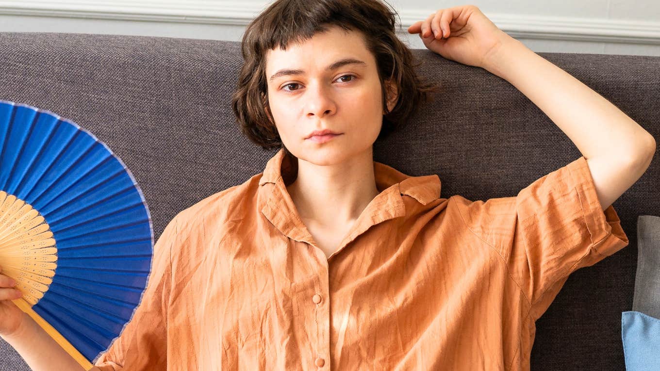 woman with zero energy looks sternly into camera holding a paper fan