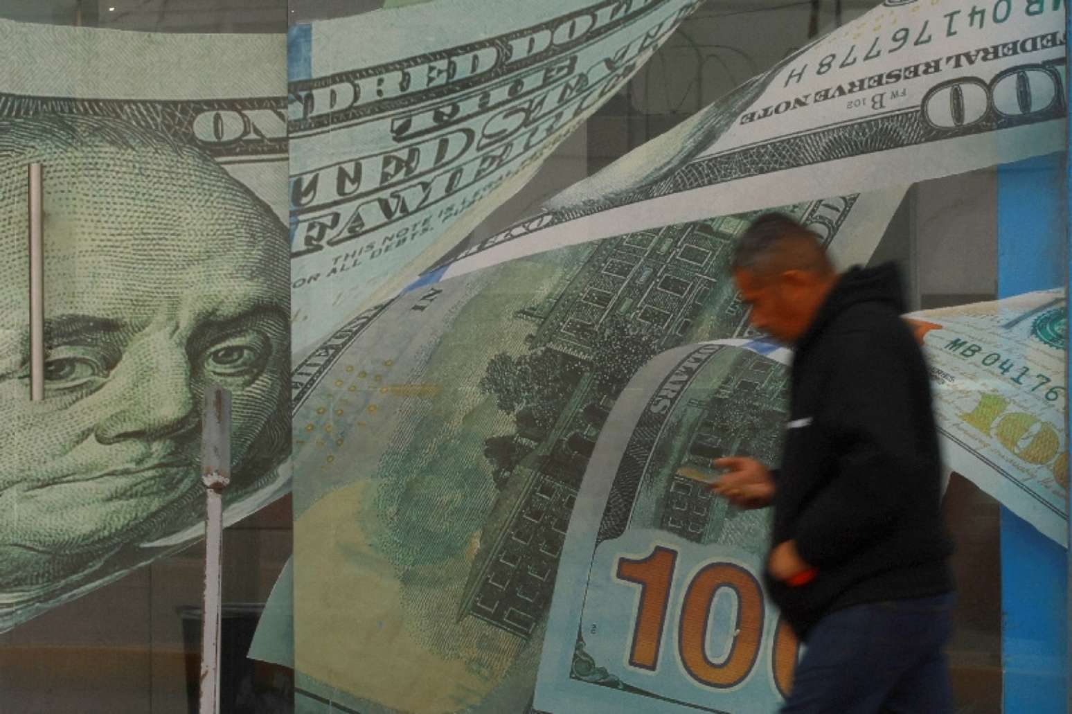 Um homem passa em frente a uma casa de câmbio, com adesivos de notas de dólar na porta e nas paredes